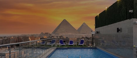 A rooftop pool with a view of the pyramids, lounge chairs, and a glass railing.