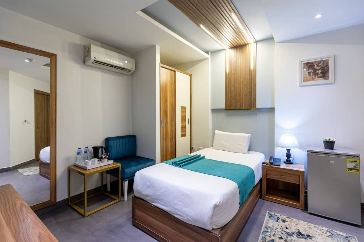 Una habitación de hotel con cama, escritorio, silla, refrigerador pequeño y aire acondicionado.
