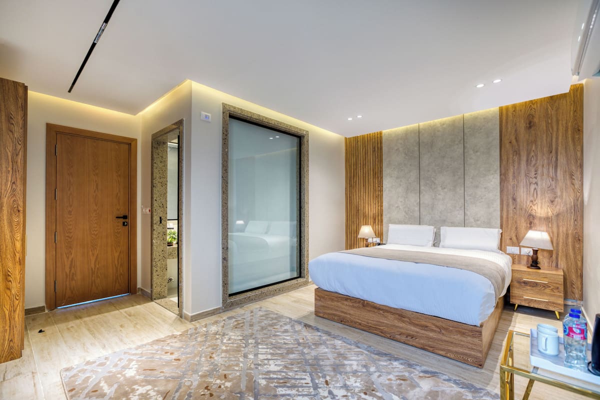 Un dormitorio moderno con una cama grande, paneles de madera, una puerta de cristal y una mesita de noche con una lámpara.