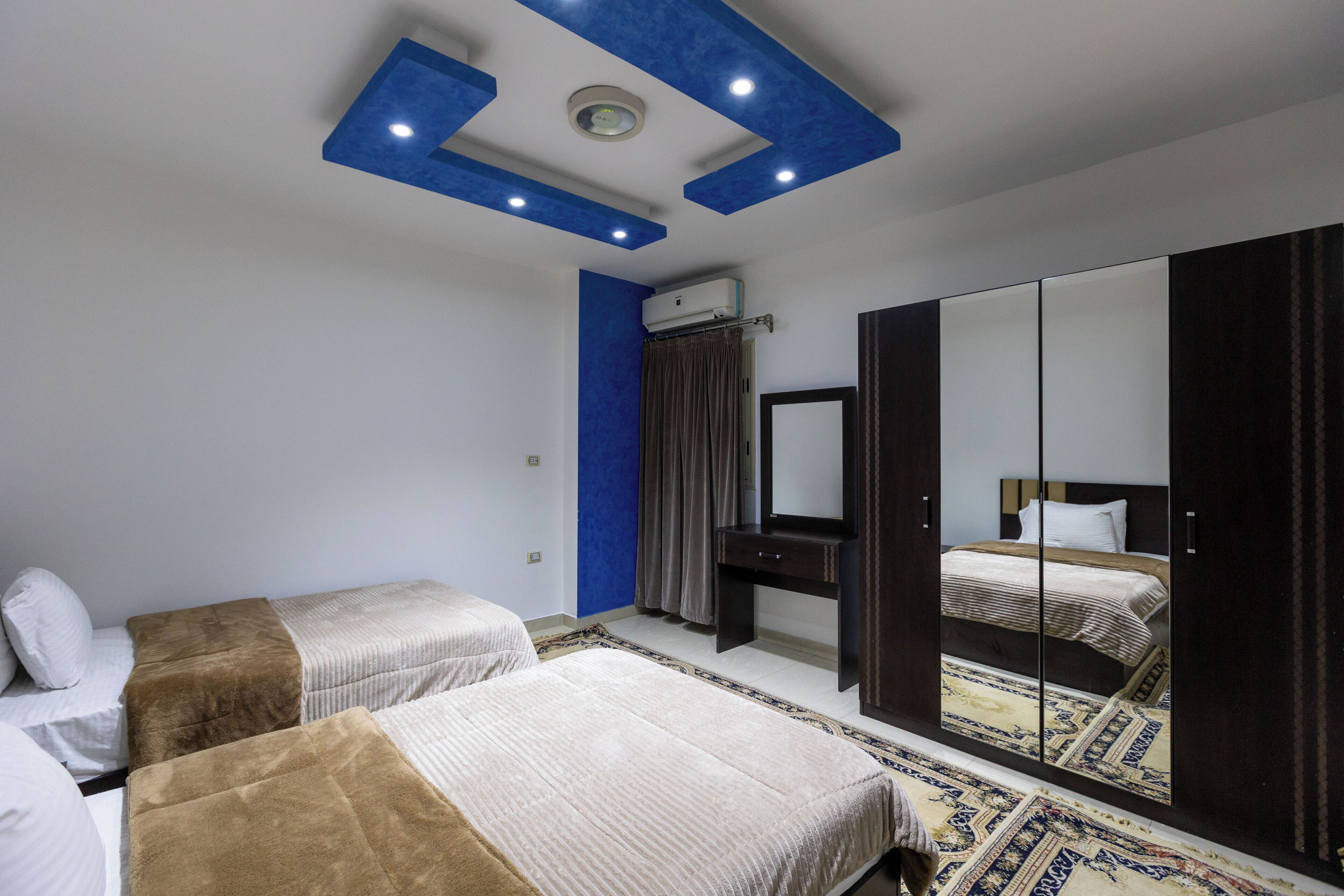 A bedroom with two beds, a large mirror, and a ceiling with blue accents.