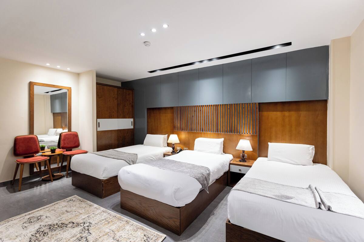 Habitación de hotel con dos camas individuales, un escritorio con silla, un espejo y una pared decorativa de madera.