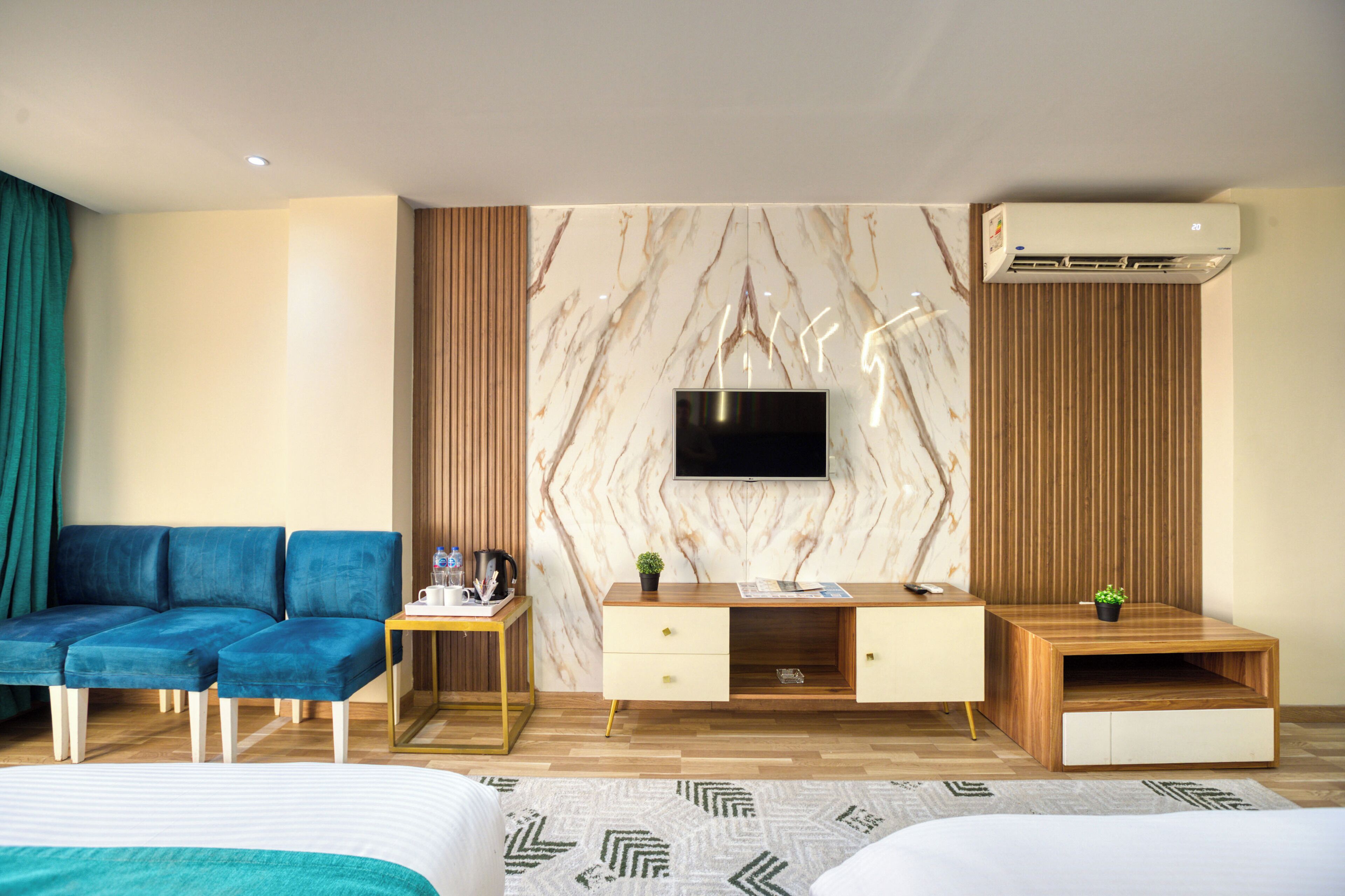 Moderni hotellihuone, jossa on sänky, sininen sohva, puinen työpöytä, televisio ja ilmastointilaite.