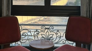 A room with two red chairs and a small round table, a window with a view of pyramids and buildings. - pyramids Yard Hotel (Giza)