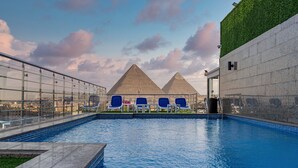 A swimming pool with blue water, surrounded by a glass wall, and two pyramids in the background. - pyramids Yard Hotel (Giza)