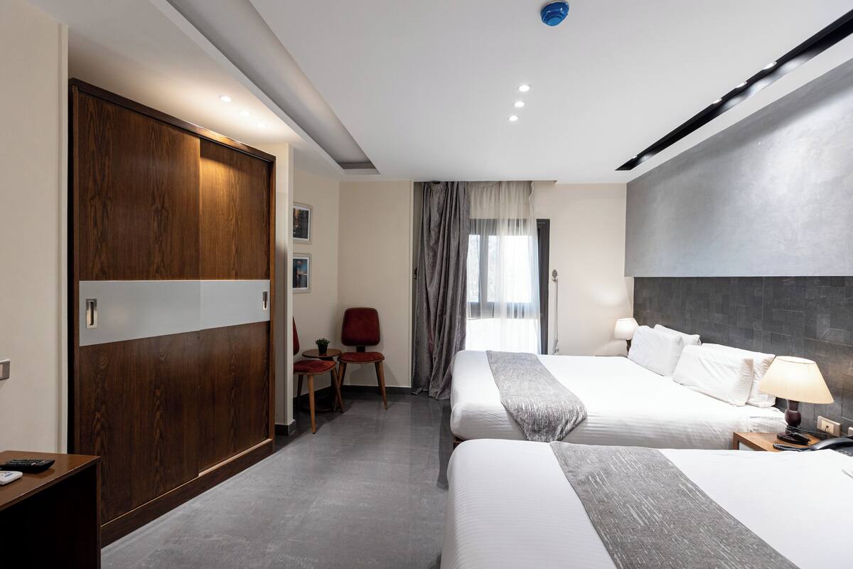 Una habitación de hotel con dos camas, un escritorio, una silla y un armario.