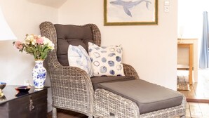 A wicker recliner with a cushion, a vase of flowers, and a framed whale painting on the wall.