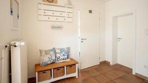 A clean, white hallway with a bench, wicker baskets, a wall-mounted shelf with decorative items, and a door.