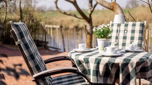 A table set outdoors with a checkered tablecloth, a potted plant, and white cups and saucers.