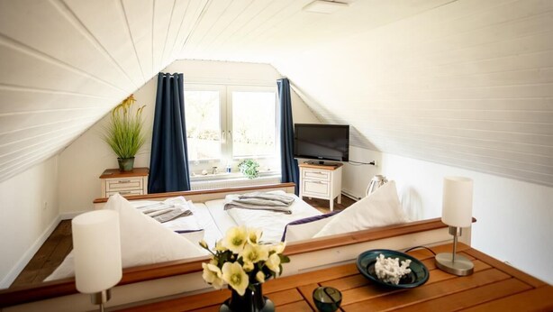 A cozy bedroom with a bed, bedside table, lamp, and a TV.