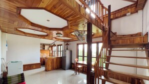 A spacious room with a high ceiling, wooden beams, a kitchen area, and a staircase. - BANSUAN Homes (Luang Prabang)