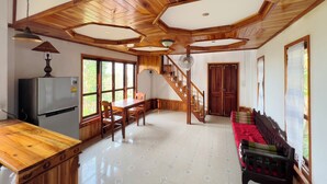 A spacious living area with a wooden ceiling, a dining table, chairs, a sofa, and a staircase leading to another level. - BANSUAN Homes (Luang Prabang)
