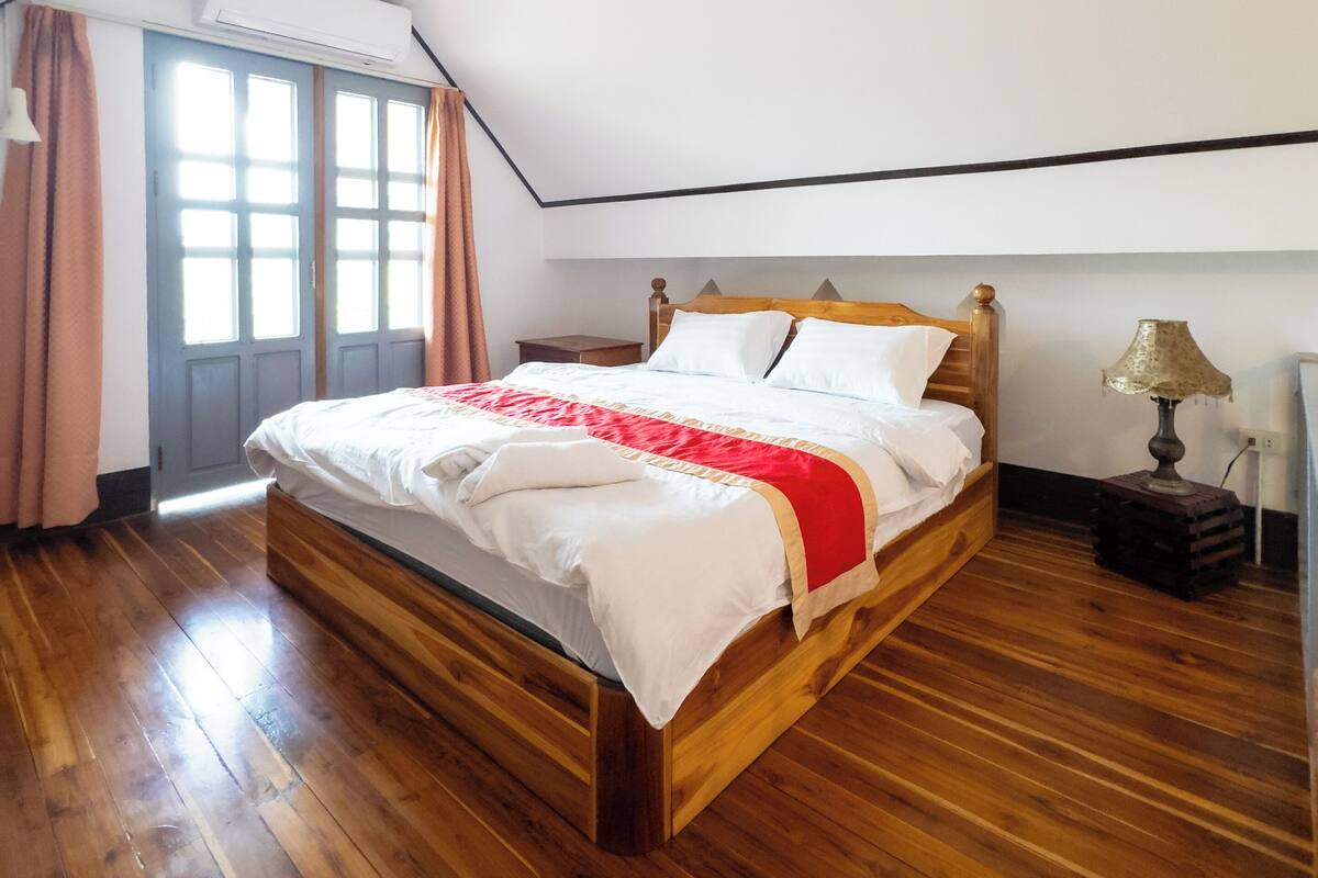 Une chambre à coucher avec un lit en bois, une table de chevet, une lampe et une fenêtre avec des rideaux.