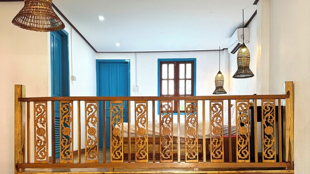 A room with a blue sofa, a wooden balcony railing, and hanging pendant lights. - BANSUAN Homes (Luang Prabang)