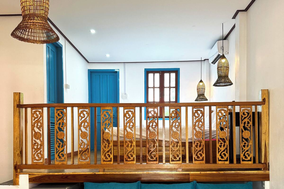 Une pièce avec un canapé bleu, une balustrade en bois et des lampes suspendues.