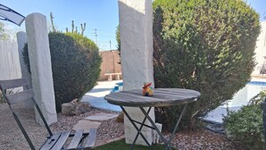Uma área de pátio com piscina, uma mesa de madeira e cadeiras.