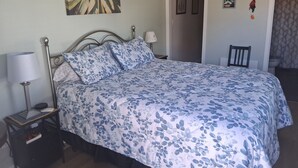 Quarto com cama, mesa de cabeceira, abajur e uma obra de arte na parede.