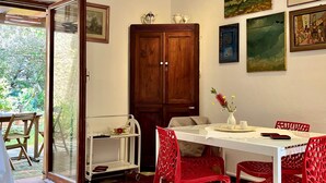 Un coin repas avec une table blanche, des chaises rouges et un buffet. Des tableaux ornent le mur et une porte donne sur l’extérieur.