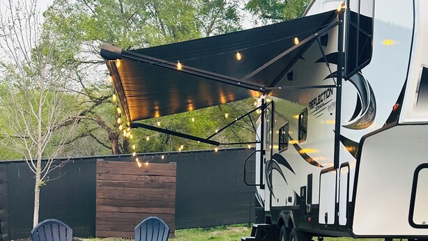 Un veicolo ricreativo con una veranda coperta, due poltrone Adirondack e luci a stringa.