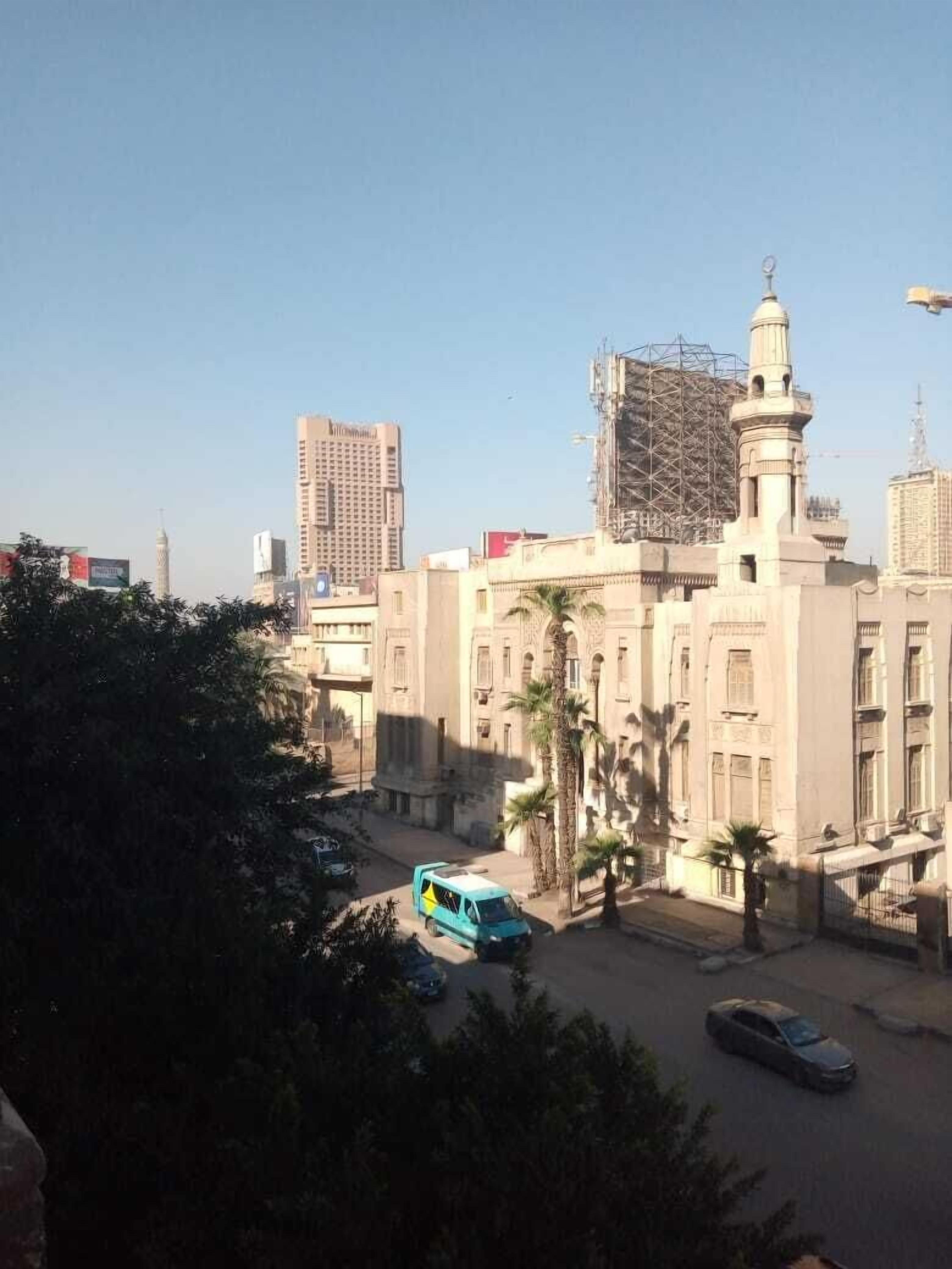 A building with a prominent minaret, surrounded by palm trees and a clear sky.