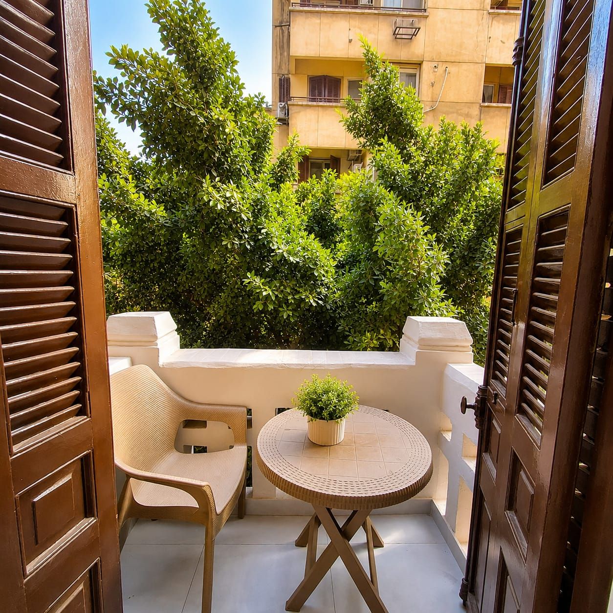 Un balcon avec une chaise et une table en osier, une plante en pot et une vue sur un immeuble doté de balcons.