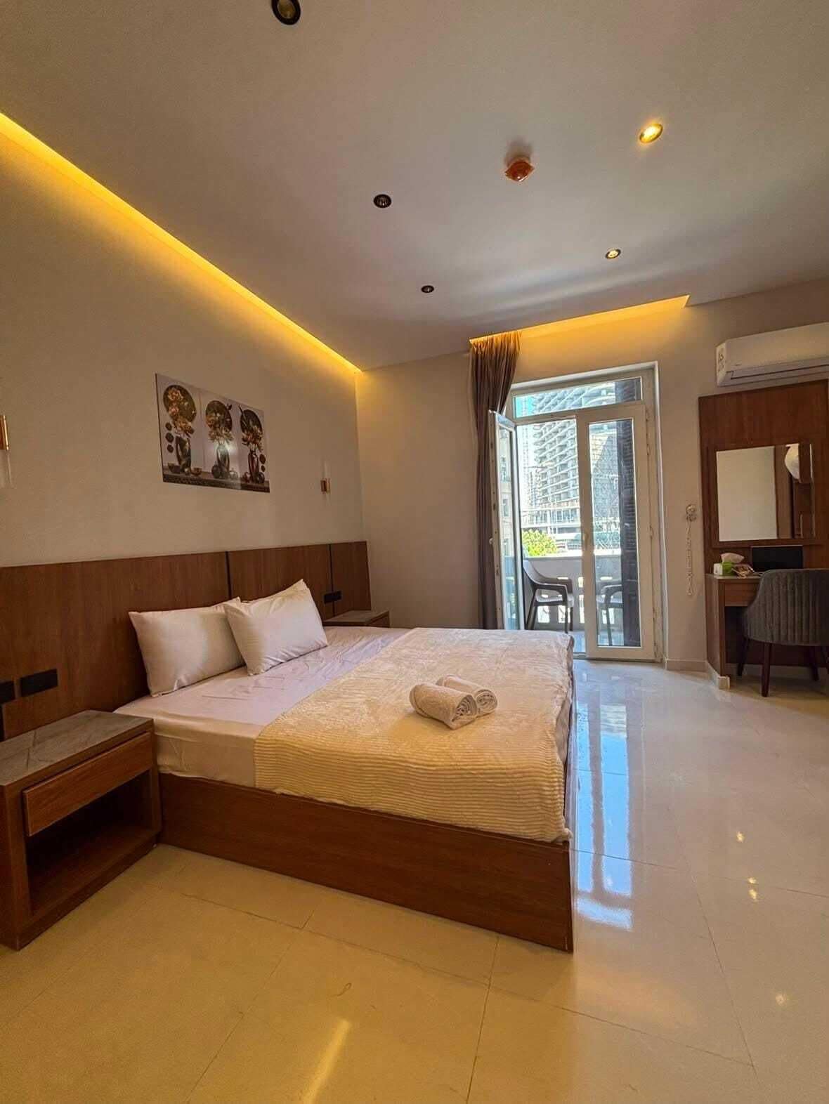 Habitación de hotel con una cama grande, un escritorio y una silla. Cuenta con una ventana con cortinas, una puerta y un equipo de aire acondicionado.