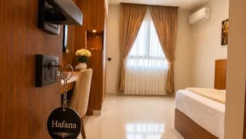 Ein Hotelzimmer mit Bett, Schreibtisch und Stuhl. Am Türgriff hängt ein Schlüsselanhänger mit dem Namen 'Hofana'.