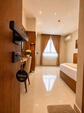 Une chambre d’hôtel avec un lit, un bureau et une chaise. Un porte-clés avec le nom « Hofana » est accroché à la porte.
