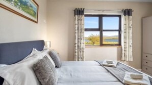A neatly made bed with pillows, a bedside table with a lamp, and a window with curtains.