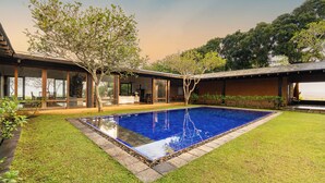 A modern house with a swimming pool, a covered patio, and a well-maintained lawn.