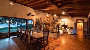 A spacious dining area with a large table and chairs, wooden flooring, and a view through large windows.