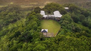 An aerial view of a secluded estate with a large lawn, a small building, and a tennis court.
