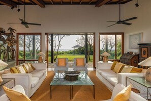 A spacious living area with a glass coffee table, white sofas, and large windows offering a view of a lush garden. - Mount Cinnamon - Exclusive Villa in Mirissa with WiFi, AC (Mirissa)