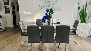A dining area with a glass table, four black chairs, a vase with blue flowers, and a large abstract painting on the wall. - Modern Getaway w/ Roku TVs in Every Room Near Beach + Downtown (St. Petersburg)