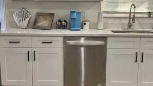A modern kitchen with white cabinets, a stainless steel dishwasher, and a window with blinds. - Modern Getaway w/ Roku TVs in Every Room Near Beach + Downtown (St. Petersburg)