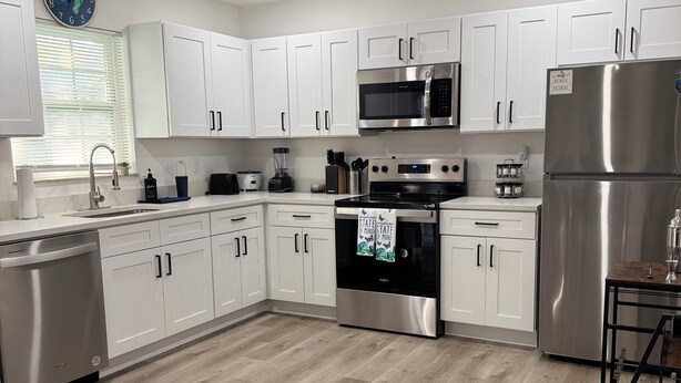 A modern kitchen with white cabinets, stainless steel appliances, and a wooden floor. - Modern Getaway w/ Roku TVs in Every Room Near Beach + Downtown (St. Petersburg)