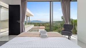 A modern bedroom with a large bed, a chair, and a balcony with a view of the landscape. - Jasmine Bophut - Stunning Seaview Villa (Koh Samui)