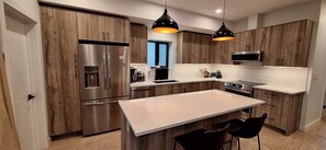 Une cuisine moderne avec des meubles en bois, des appareils électroménagers en acier inoxydable et des luminaires suspendus.