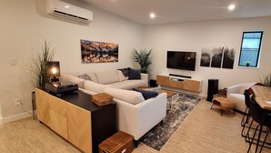 A modern living room with a sofa, TV, and dining area. - The Orange Bridge Lookout | Modern 2BR | Walk to Everything (Nelson)