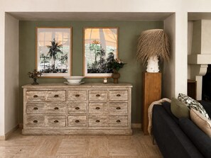 A room with a wooden dresser, two framed pictures, a tall vase, and a sofa.