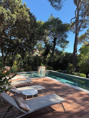 A pool area with wooden deck, lounge chairs, and a stone feature.