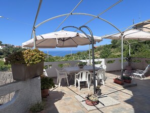 A patio with a table and chairs under umbrellas, potted plants, and a view of the sea.