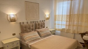 Une chambre à coucher avec une tête de lit capitonnée, une couvre-lit matelassée, deux tables de chevet ornées de lampes décoratives et une fenêtre avec des rideaux.