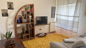 Un salon avec un canapé, un téléviseur, une bibliothèque en bois, un tapis à motifs et une plante en pot.
