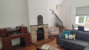 Uma sala de estar com lareira, uma escrivaninha, um sofá e uma escada.
