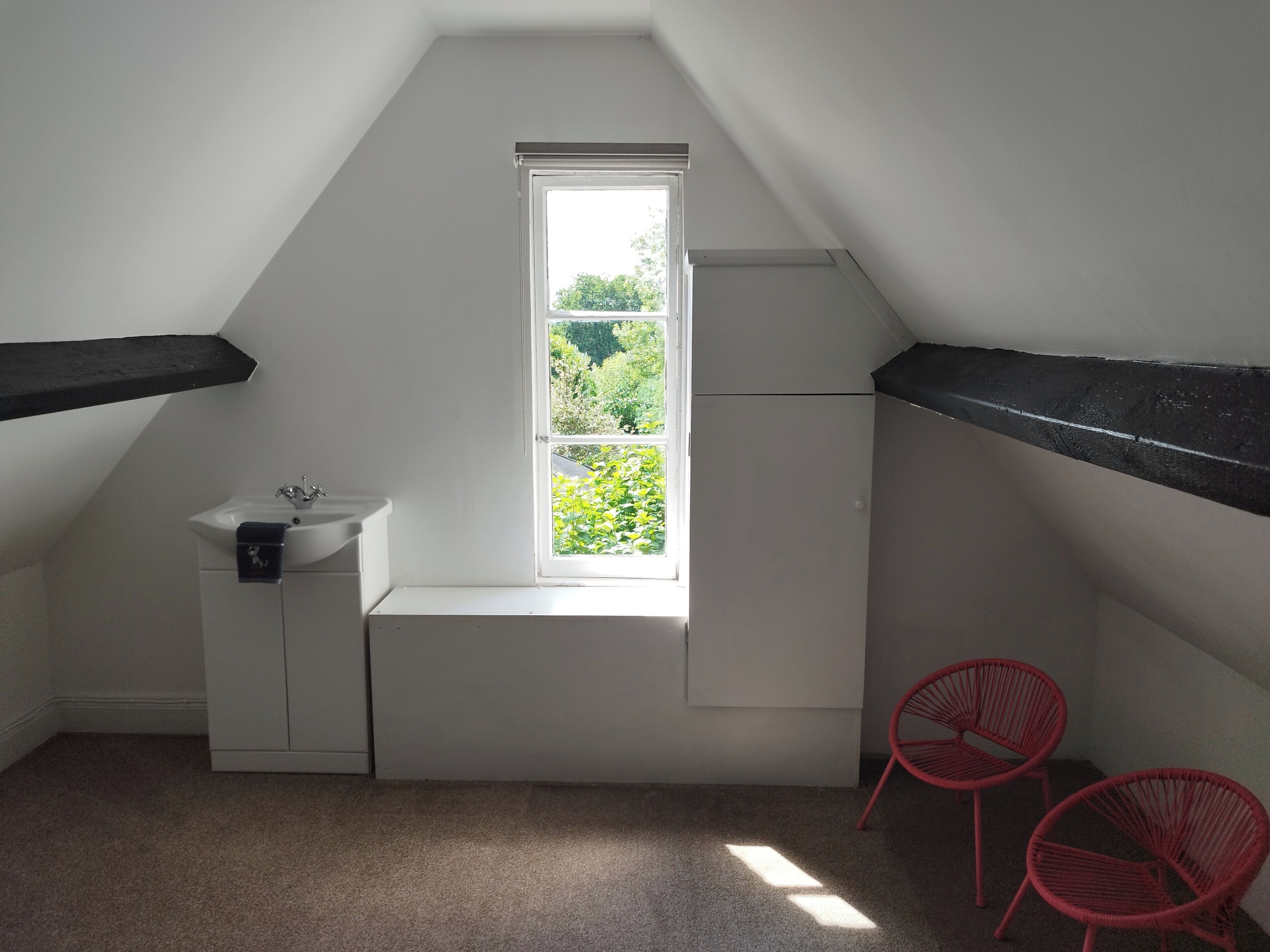 A small, white room with a window, a sink, and two red chairs.