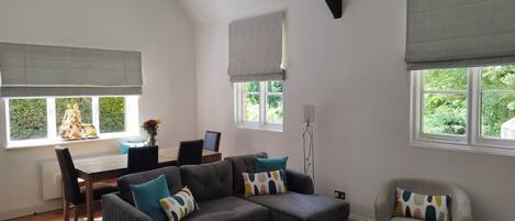 A modern living room with a sectional sofa, a small table, and a dining area with a chair and a vase of flowers.