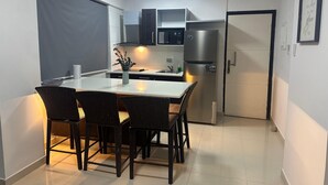 Een kleine keuken met een eethoek, met een koelkast, kastjes en een tafel met stoelen.