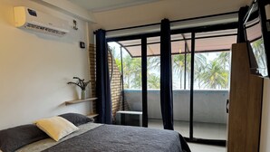 Een slaapkamer met een bed, een televisie, een kledingkast en een balkon met uitzicht op palmbomen.