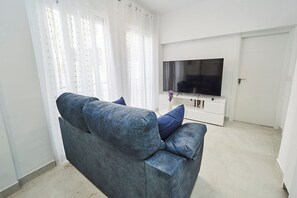 A living room with a grey sofa, a flat-screen TV on a white stand, and a door in the background. - Csa Isolde: Cozy and Modern (Nerja)