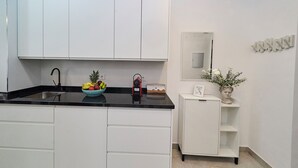 Une cuisine moderne avec des meubles blancs, un plan de travail noir et un panier de fruits.